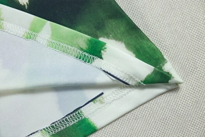 Macro shot of overlock stitching and green watercolor floral print on textured fabric