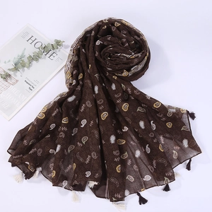 Detail of dark brown paisley linen scarf with fringes and eucalyptus leaves on a white surface