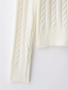 Close-up of chunky cable knit pattern and ribbed cuff detail on a white sweater
