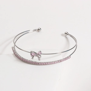 Close-up of silver bow bracelet featuring pink zircon stones on white stone background