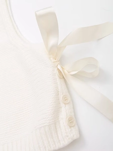 Detail of cream knit vest featuring side buttons and elegant silk ribbon bow tie