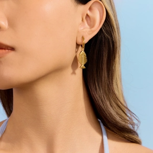 Détail d'une boucle d'oreille arête de poisson dorée sur mannequin, fini métallique