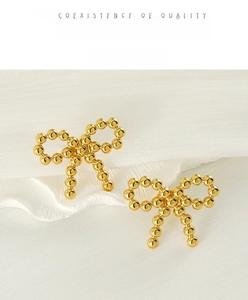 Macro shot of 18k gold plated beaded bow earrings on elegant white silk background