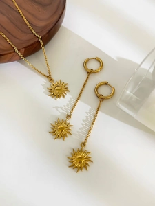 Detail of 18K gold-plated sun pendant necklace and earrings set on minimalist background