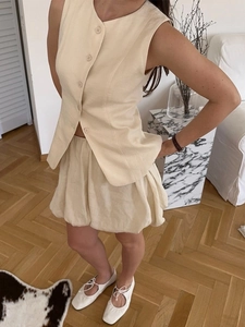 Détail d'un gilet sans manches crème et d'une jupe courte bouffante en mélange de lin