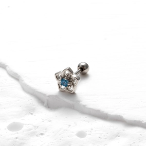 Close-up of flower stud earring with blue zircon on white textured stone background