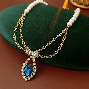 Detail of vintage necklace with pearl strand, gold chain and blue bow pendant