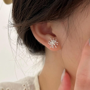 Detailed view of fireworks snowflake shaped silver stud earrings on female model's earlobe