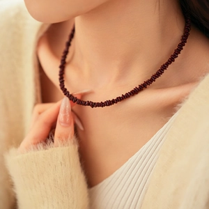 Detalle de collar de cuentas de piedra irregular rojo oscuro en el cuello