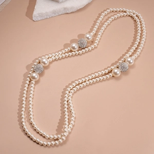 Detail view of double-layered pearl necklace with crystal pave disco balls on beige surface