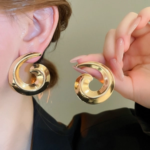 Macro detail of large gold spiral earrings featuring a polished mirror finish on model