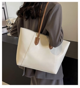 Close-up of a white tote bag with brown straps and detailed stitching in a modern setting