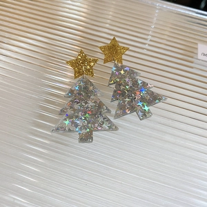 Close-up of golden glitter star earrings with holographic Christmas tree charms