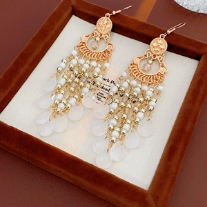 Macro detail of ethnic long gold tassel earrings with white beads and crystal drops