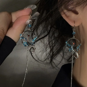Détail des boucles d'oreilles grue en argent avec émail bleu et longues franges en métal