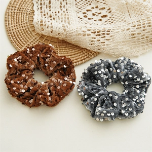 Brown and grey sequin velvet scrunchies displayed on a natural woven mat for hair styling