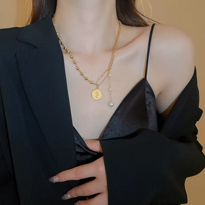 Detail of layered gold coin necklace with paperclip chain and faux pearl on a model