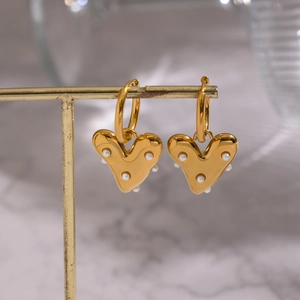 Boucles d'oreilles cœur dorées avec perles blanches sur présentoir en marbre chic