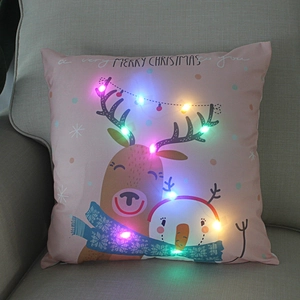 Detail of pink Christmas pillow with reindeer and glowing LED lights on beige sofa