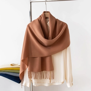 Dettaglio di una sciarpa marrone effetto cashmere con frange su una camicia beige