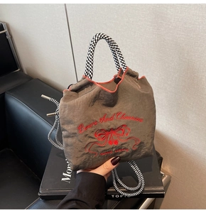 Detail of dark grey nylon handbag with red cherry embroidery and woven cord handles