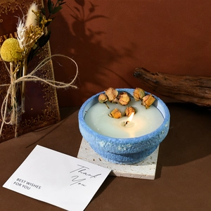 Blue ceramic scented candle jar with dried rose buds and flame on a vintage wooden base