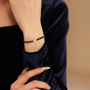 Detail of gold bracelet with deep blue gemstone and white zircon flower on woman's wrist