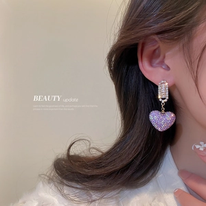 Elegant gold-tone heart drop earrings with purple crystals on a model's ear