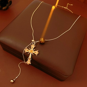 Detail of tiger eye bead and crystal cross pendant on gold snake chain necklace