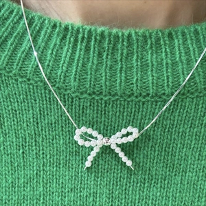 Minimalist 925 sterling silver necklace featuring a pearl bow pendant on a green sweater