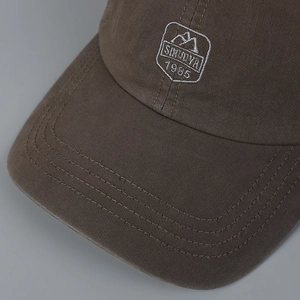 Detail of dark brown cotton baseball cap showing white Sinuoya 1985 embroidery and stitching