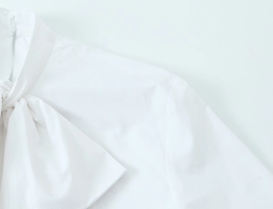 Close-up of white high-neck shirt featuring bow tie and back collar button detail