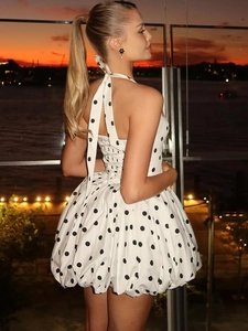 White polka dot halter dress with backless design and flowing hem against city sunset