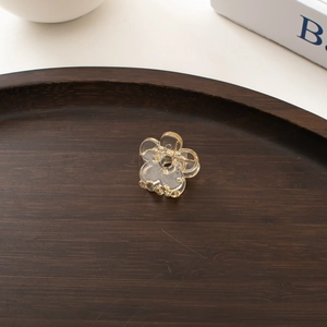 Detailed view of a transparent mini flower hair clip on a premium wooden tray