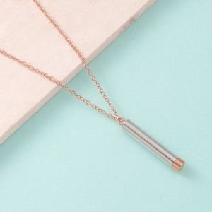 Detailed view of two-tone cylindrical stainless steel pendant on a rose gold chain necklace