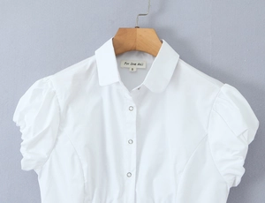 Detail of white puff sleeve shirt featuring silver snap buttons and a minimalist collar