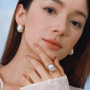 Elegant gold-framed pearl earrings and ring set worn by model on blue background