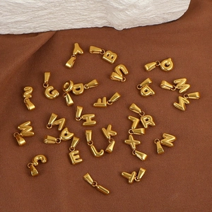 Polished 18K gold stainless steel bubble letter pendants displayed on textured stone