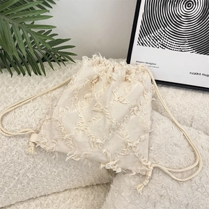 Close-up of beige canvas backpack with textured fringe diamond pattern and drawstring detail