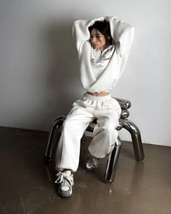 Dettaglio del set felpa bianca con mezza zip e pantaloni con scritte su sedia in metallo