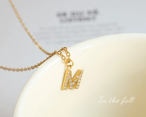 Macro detail of gold letter M pendant necklace with shimmering zircon stones on porcelain