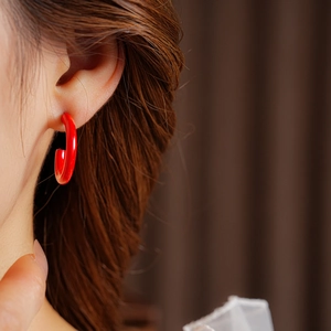 Close-up of red C-shaped enamel hoop earrings worn by a model with a glossy metal finish