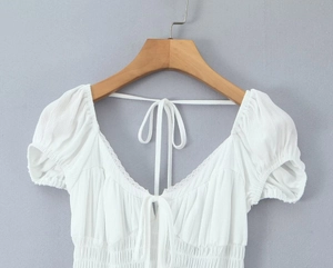 Detail of white V-neck pleated top with puff sleeves and front tie closure