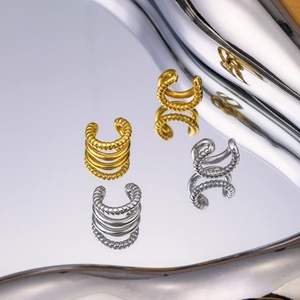 Twisted C-shape gold and silver titanium steel earrings on a reflective mirror surface