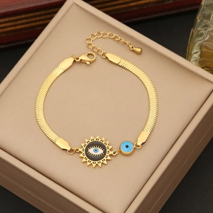Macro shot of gold snake chain bracelet with evil eye charm on beige jewelry box