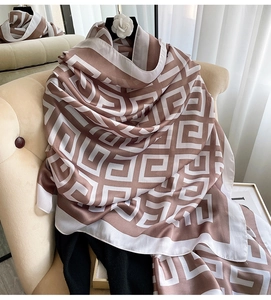 Detail of silk-like scarf with geometric G-pattern draped on a chair with camellia