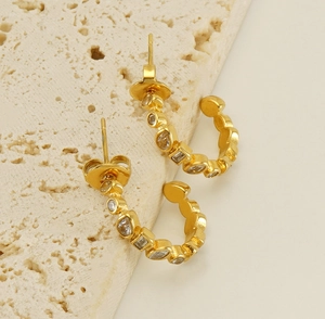 Detail view of 18k gold C-shaped earrings with inlaid cubic zirconia on travertine base