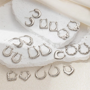 Detailed collection of silver stainless steel earrings and hoops on white stone and silk