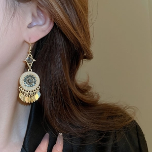 Detailed close-up of Bohemian gold drop earrings with leaf pendants and green bead inlay