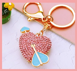Detail of heart keychain with pink rhinestones and blue enamel arrow on gold metal base